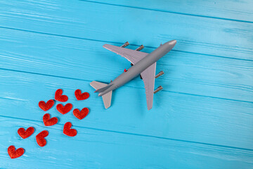 Top view of toy passenger boeing plane with red hearts. Blue wooden desk surface.