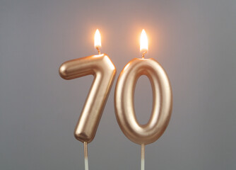 Burning gold birthday candles on gray background, number 70