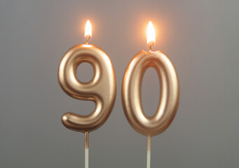 Burning gold birthday candles on gray background, number 90