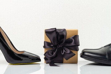 Still life of gift box with black ribbon and shoes. Classic black mens and womens footwear isolated on white.