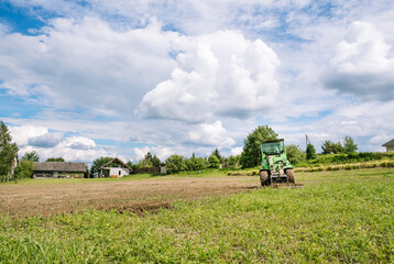 Fototapeta premium A green mini skid steer loader clear the construction site. Land work by the territory improvement. Small tractor with a ground leveler for moving soil, turf. Machine for agriculture work. Copy space