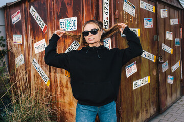 City portrait of beautiful young female wearing black blank hoodie and blue jeans with space for...