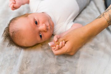 New family member. Closeup indoor shot of a dark-haired and dark-eyed caucasian baby boy touching his mother's thumb with all of his little hand. Parent-child relationship. High quality photo