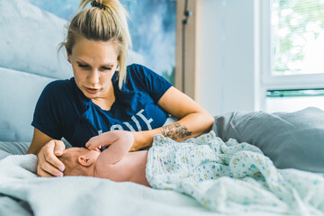 Blond white mother lying in bed with baby boy caressing his head and shushing him to calm him down. Responsibility. Motherhood. Horizontal indoor shot. High quality photo