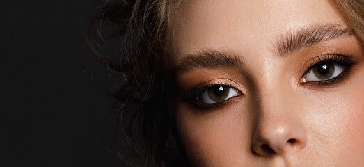 Young beauty with well-groomed eyebrows and professional make-up on a black background, close-up