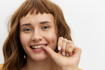 Fototapeta premium a happy, joyful woman stands on a white background in a yellow T-shirt playfully holding her finger near her mouth