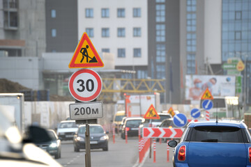 Roadworks warning traffic signs of construction work on city street and slowly moving cars