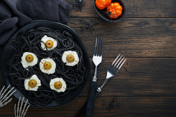 Halloween party Italian black pasta decorated horror  olives like eyes on black plate on old dark table background. Monster face from pasta. Halloween decorations and Halloween food concept. Mock up.