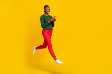 Naklejka na ściany i meble Full length photo of sweet pretty lady dressed green shirt jumping high chatting gadget empty space isolated yellow color background