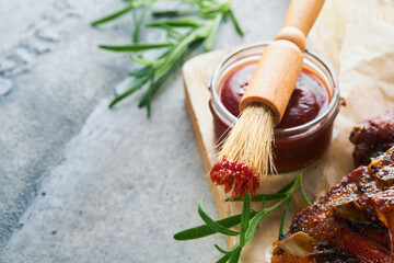 Hot and spicy barbecue sauce in jar bowl with basting brush on old stone gray background. Flat lay...