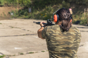 back view of a man practicing aiming at the shooting range and holding a black rifle with a...