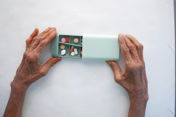 senior women taking medical pills from a pill box on white background 