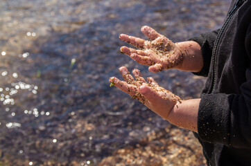 Dirty hands of a toddler playing with sand, water and stones at a beach