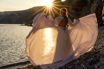 A mysterious female silhouette with long braids stands on the sea beach with mountain views, Sunset...