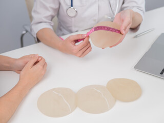 A plastic surgeon measures breast implants with a centimeter tape and demonstrates to a female...