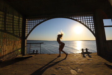 Beautiful blonde girl dances on the seashore near landing stage.