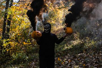  A portrait of a creepy scary man in skeleton mask. Monster holding burning pumpkins jack-o-lantern...