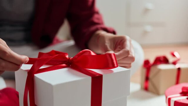 Female hands are packing a gift for christmas, preparing a gift box for a wedding anniversary, Holiday day girl tying a red bow on a white gift box. Valentine's Day preparation packaging
