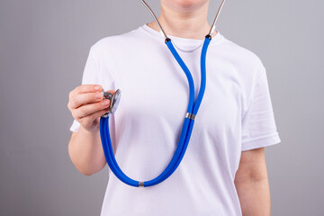 A medical worker without a face holds a stethoscope in his hand on a gray background