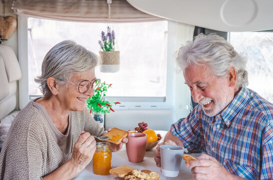 Cheerful laughing senior couple in travel vacation leisure inside a camper van dinette enjoying breakfast together.