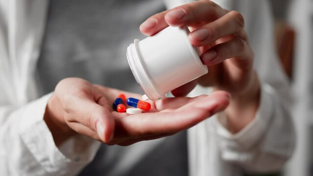 Female hands pour out pills from a bottle box, Close-up capsule pills fall into the palm of the hand, priming tablets of sedative painkillers depression headache
