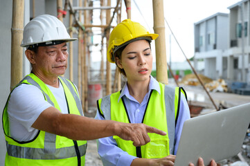 Construction woman and foreman in vest with helmet working with laptop, standing on under-construction building site. Home building project. Engineer foreman discusses with a coworker at workplace