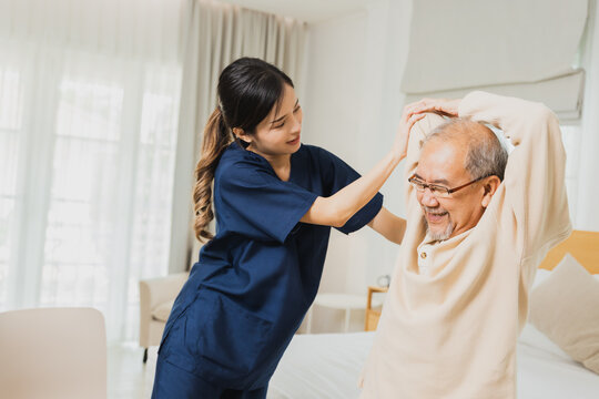 female physiotherapist helping senior man exercise, helping elderly male patient on bed in morning 