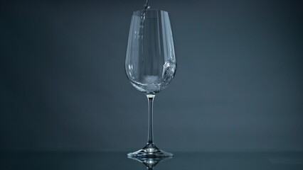 Water pouring wine glass at dark background closeup. Clear liquid splashing