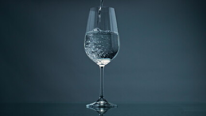 Pure water filling glass at dark background closeup. Bubbles rising transparent