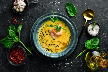 Autumn menu. Pumpkin soup with shrimp, olive oil and sesame seeds. In a blue bowl. On a black stone background.