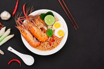 Tom Yum Goong Instant Noodle Ramen - Asian Style Thai and Chinese are spicy. placed on a black wooden table With seafood shrimp, lime, red chili, garlic, galangal, lemongrass, kaffir lime stand