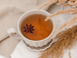 Closeup of porcelain cup of tea with anise on marble table with pampas grass, aesthetic minimal...