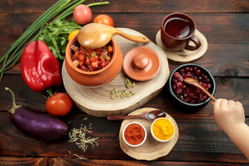 Rustic still life with a pot, wooden spoon, autumn vegetables, wooden table, dark wood. The hand holds a spoon.
