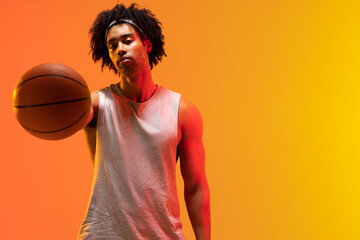 Image of biracial basketball player with basketball on orange to yellow background
