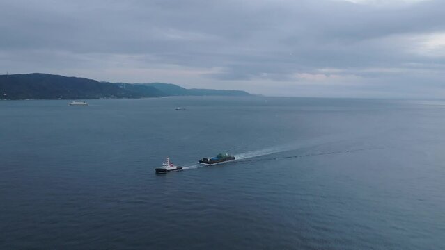 Flying toward small tug boat pulling barge through coastal waters at dusk