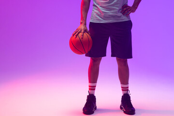 Image of low section of biracial basketball player with basketball on neon purple background - Powered by Adobe