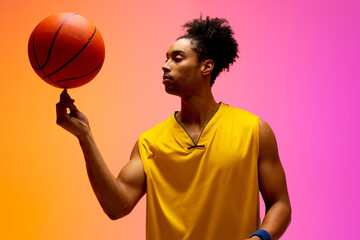 Image of biracial basketball player spinning basketball on pink to orange background