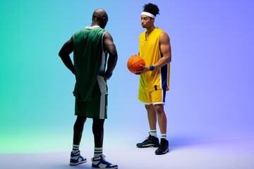 Fototapeta premium Image of two diverse basketball players with basketball on purple to green background
