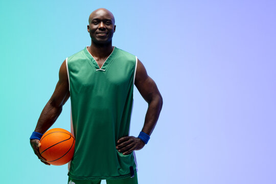Image of smiling african american basketball player with basketball on green to blue background