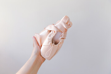 Ballerina dancer hand holding new pastel beige ballet shoes with satin ribbon isolated on white background. Ballerina classical pointe shoes for dance training. Ballet school concept. Copy space