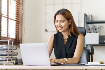 Asian thai businesswoman using laptop at working desk in modern office, busy job but feeling happy.