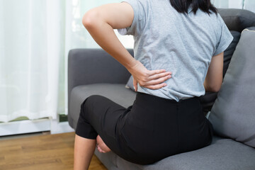Fototapeta premium Asian woman aching back spinal pain from stress of injury, painful ache stress muscle cramp, body upper muscle problem, indeed of medical physical therapy concept, home living room coach lifestyle