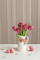 Bouquet of pink tulips in a vase jug on the background of a gray wall. Macaroons sweets