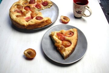 Slice of sweet plum pie and coffee on white background