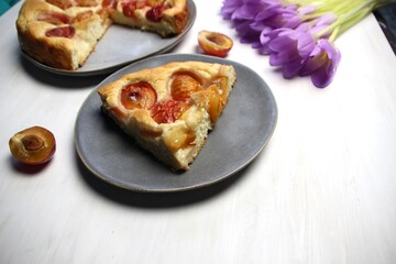 Plum cake on plate, pink crocus flowers, cup of coffee on white background