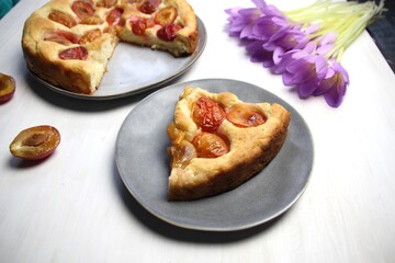 Plum cake on plate, pink crocus flowers, cup of coffee on white background