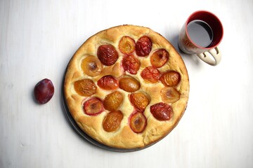 Plum cake on plate with fruit, cup of coffee on white wooden table