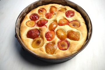 Hot plum cake in baking pan, just from oven, on white background