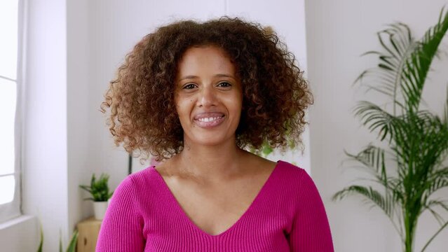Portrait of happy african woman with curly hair smiling at camera standing indoors. Authentic female ethiopian student. High quality 4k footage