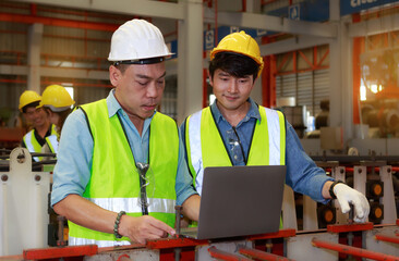 Asian male Hard Hat chief engineer using laptop to train workers to check checks heavy metal machinery